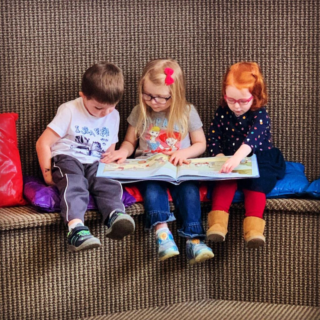 Three kids sit together reading a book